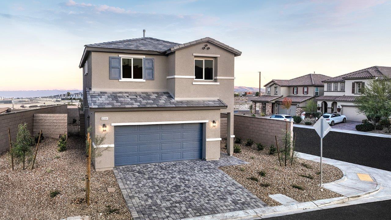 Our model home in the Meranto Bay community with tan and blue exterior paint schemes, a flat tile roof, front yard landscaping, and paver walkways.