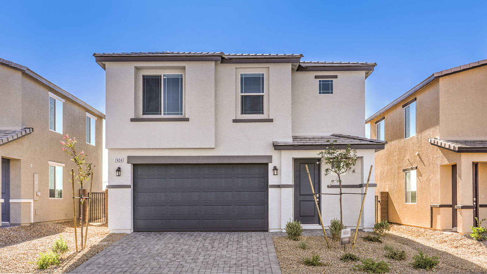 Our 1550 model home in the Heartland Cottages community with white and tan exterior paint schemes, a flat tile roof, front yard landscaping, and paver walkways.