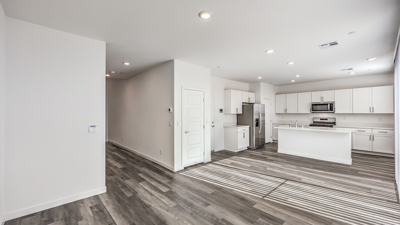 The Heartland Cottages 1550 Plan open concept Great Room with LVP panel flooring, two large windows, and a sliding door to the backyard.