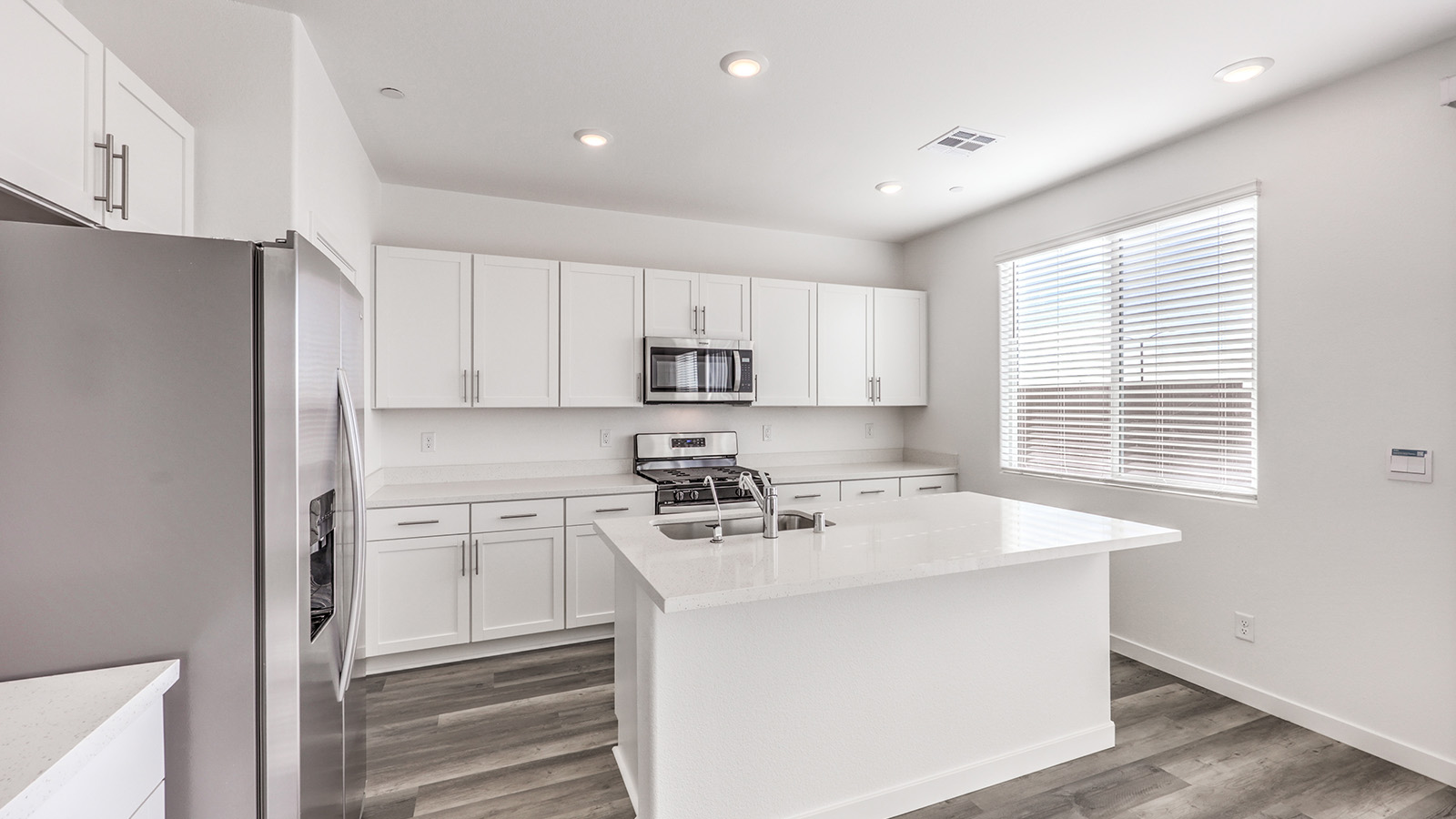 Our 1550 model kitchen in the Heartland Cottages Community with white shaker style cabinets, Granite Slab countertops, a kitchen island, and Whirlpool Stainless Steel appliances.