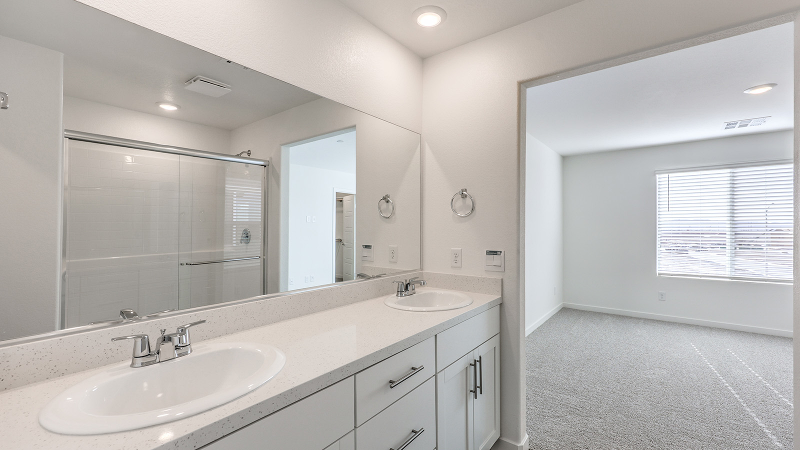 Attached to the Bedroom One Suite, our 1550 model bathroom with granite countertops at the double Bath Vanity, a walk-in shower, mirror, and white cabinets.