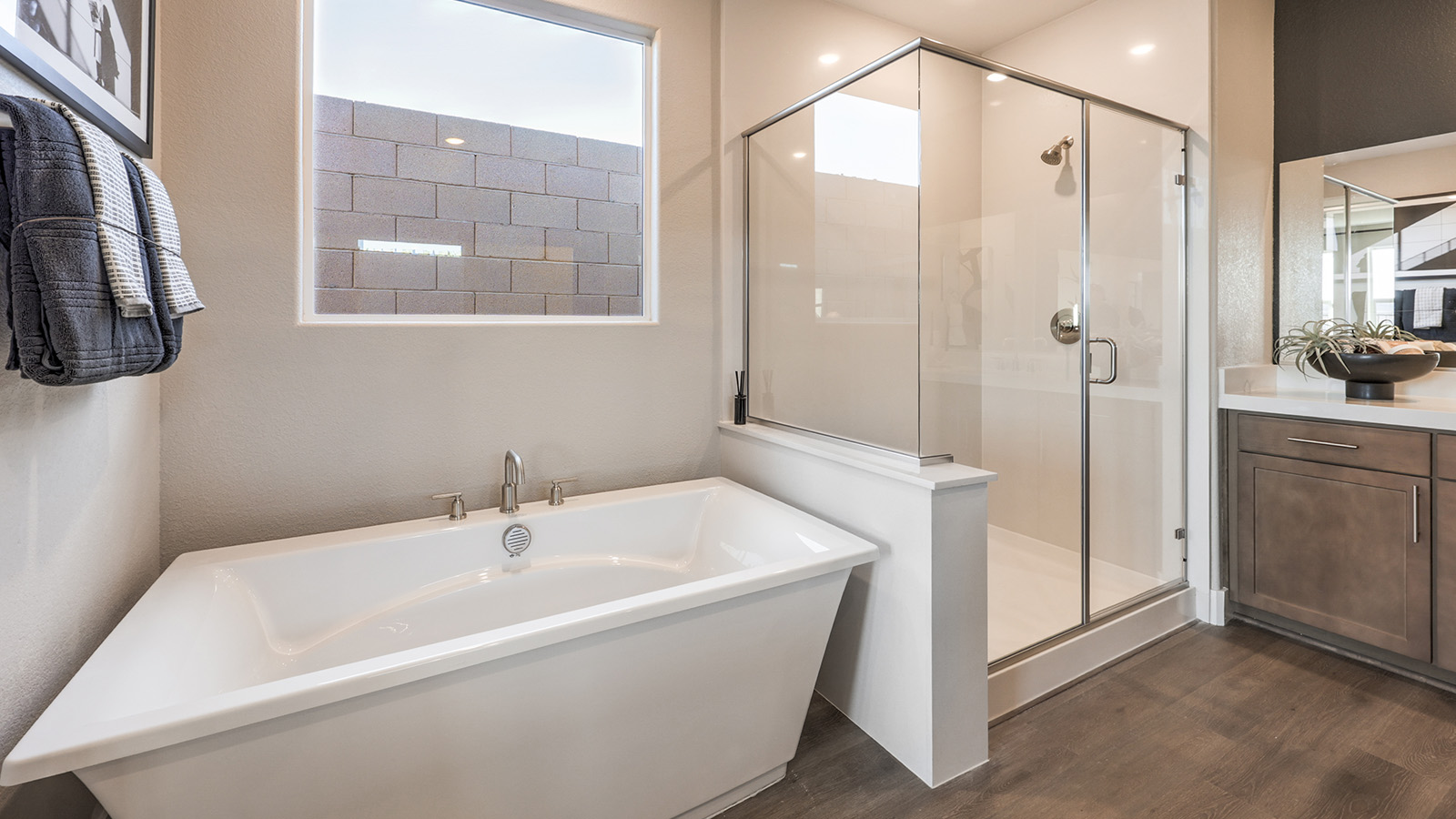 The Majestic Hills 2390 Plan Main Bedroom Suite Bathroom featuring Luxury Vinyl Plank flooring, a separate soaking tub with granite surround, and a walk-in shower with a clear glass enclosure. This spacious layout offers a spa-like retreat with private access to large walk-in closets, blending comfort and elegance.