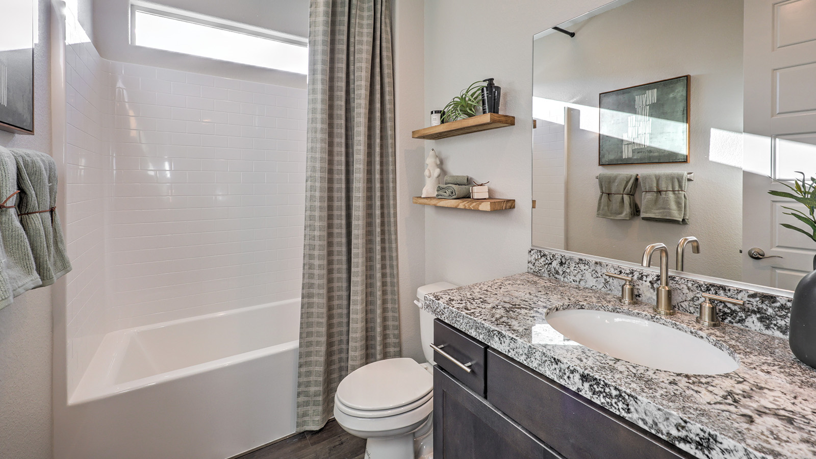 The Majestic Hills 2650 Plan Bathroom 3 featuring Luxury Vinyl Plank flooring, a granite countertop vanity with undermount sink, and a combination tub and shower with white tile surround. A high transom window allows natural light while maintaining privacy, making this bathroom both functional and inviting for guests or family members.