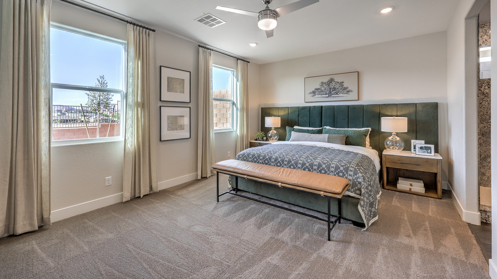The Majestic Hills 2650 Plan Main Bedroom Suite featuring plush wall-to-wall carpet, multiple windows providing natural light, and a modern ceiling fan. This spacious layout offers a private retreat with direct access to the ensuite bathroom and walk-in closet, designed for comfort and relaxation.