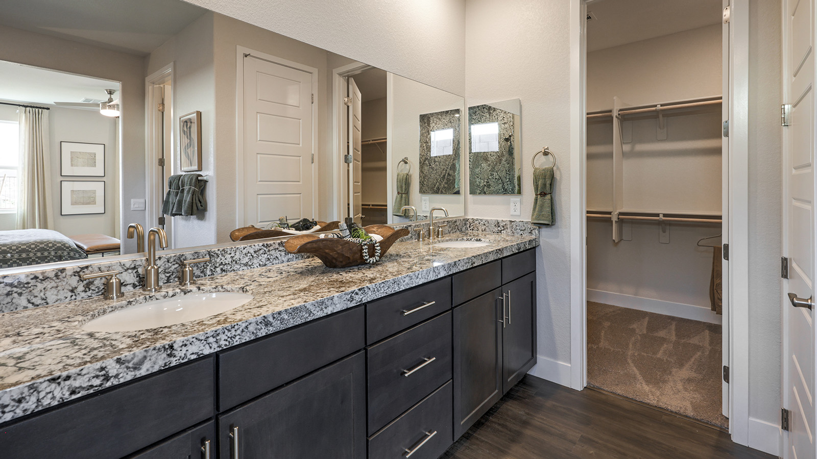 The Majestic Hills 2650 Plan Main Bedroom Suite Bathroom featuring Luxury Vinyl Plank flooring, granite countertops at the dual-sink vanity, and direct access to large walk-in closets. This spacious bathroom offers modern functionality with ample storage and natural light, creating a private and relaxing retreat.