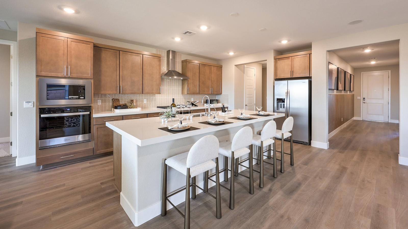 The Majestic Hills 2390 Plan Kitchen featuring Luxury Vinyl Plank flooring, granite countertops with a large center island, and a herringbone tile backsplash. Equipped with Whirlpool Stainless Steel Appliances including a 5-burner cooktop, built-in microwave, and dishwasher, this kitchen is designed for both functionality and modern style.
