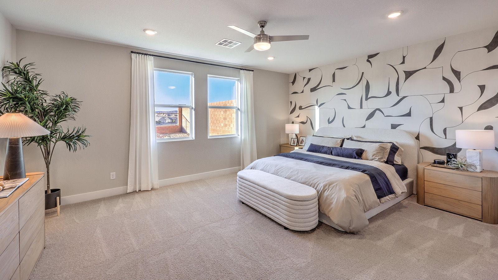 The Majestic Hills 2390 Plan Main Bedroom Suite featuring plush wall-to-wall carpet, multiple windows providing natural light, and a modern ceiling fan. This spacious layout offers a private retreat with direct access to the ensuite bathroom and walk-in closet, designed for comfort and relaxation.