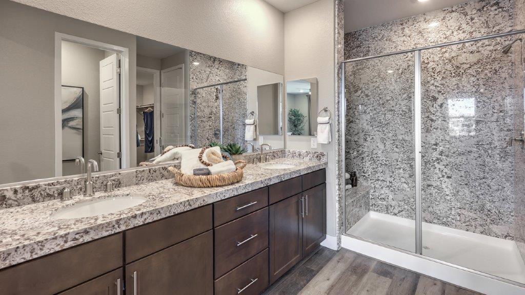 Attached to the Bedroom One Suite, our 1870 model bathroom with quartz/marble fusion countertops at the double Bath Vanity, a walk-in shower, walk-in closet, mirror, and brown cabinets.