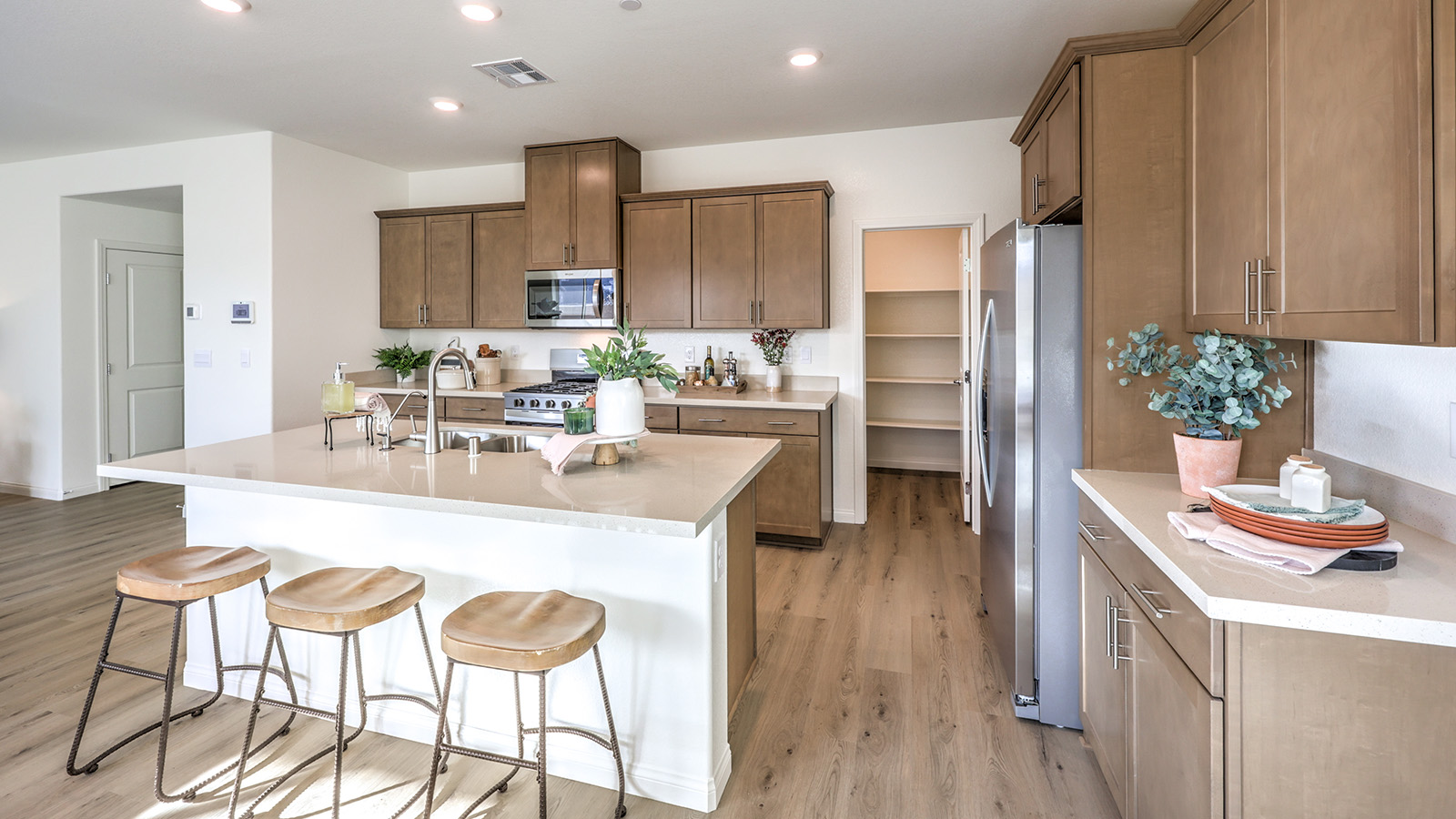 Our 2436 model kitchen in the Sky Falls Community with brown shaker style cabinets, Quartz Slab countertops, a kitchen island, and Whirlpool Stainless Steel appliances.