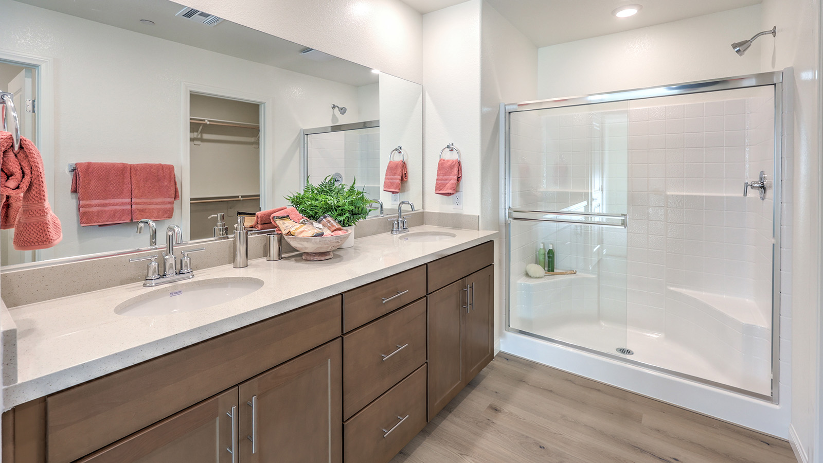 Attached to the Bedroom One Suite, our 2436 model bathroom with quartz/marble fusion countertops at the double Bath Vanity, a walk-in shower, walk-in closet, mirror, and brown cabinets.