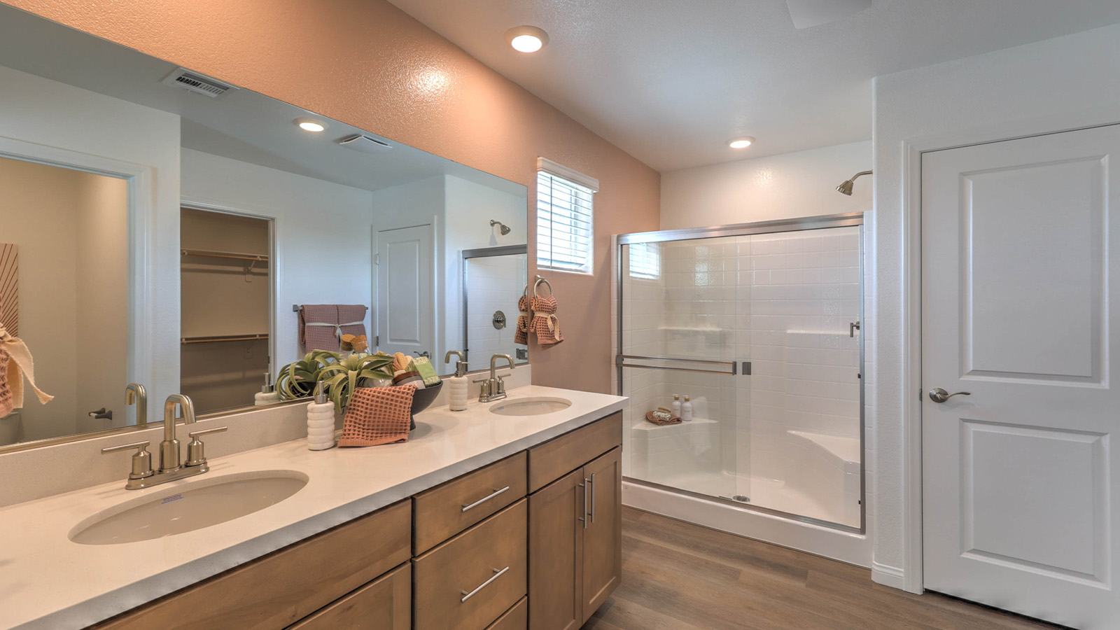 Attached to the Bedroom One Suite, our 2660 model bathroom with quartz countertops at the double Bath Vanity, a walk-in shower, walk-in closet, mirror, and brown cabinets.