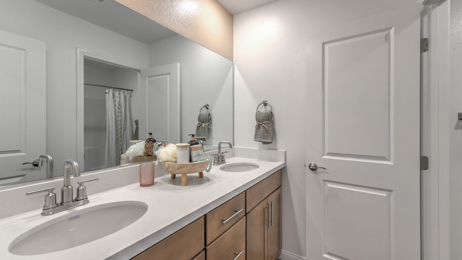 Bathroom Two in our Sky Falls  2660 model with quartz countertops at the double Bath Vanity, a walk-in shower, mirror, and brown cabinets.