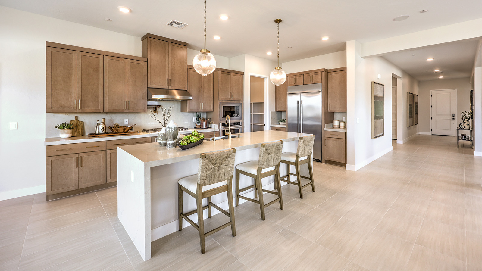 The kitchen in our Heartland Manor 2754 Plan features luxury vinyl plank flooring, an open-concept design, and a spacious layout. A large island with seating provides ample counter space, complemented by quartz or granite countertops with a 2¼-inch edge. Whirlpool stainless steel appliances include a five-burner cooktop, built-in ovens, a microwave, and a dishwasher. The space also features 42-inch upper cabinets for extra storage and a walk-in pantry for added convenience. Large windows bring in natural light, creating a bright and inviting atmosphere.