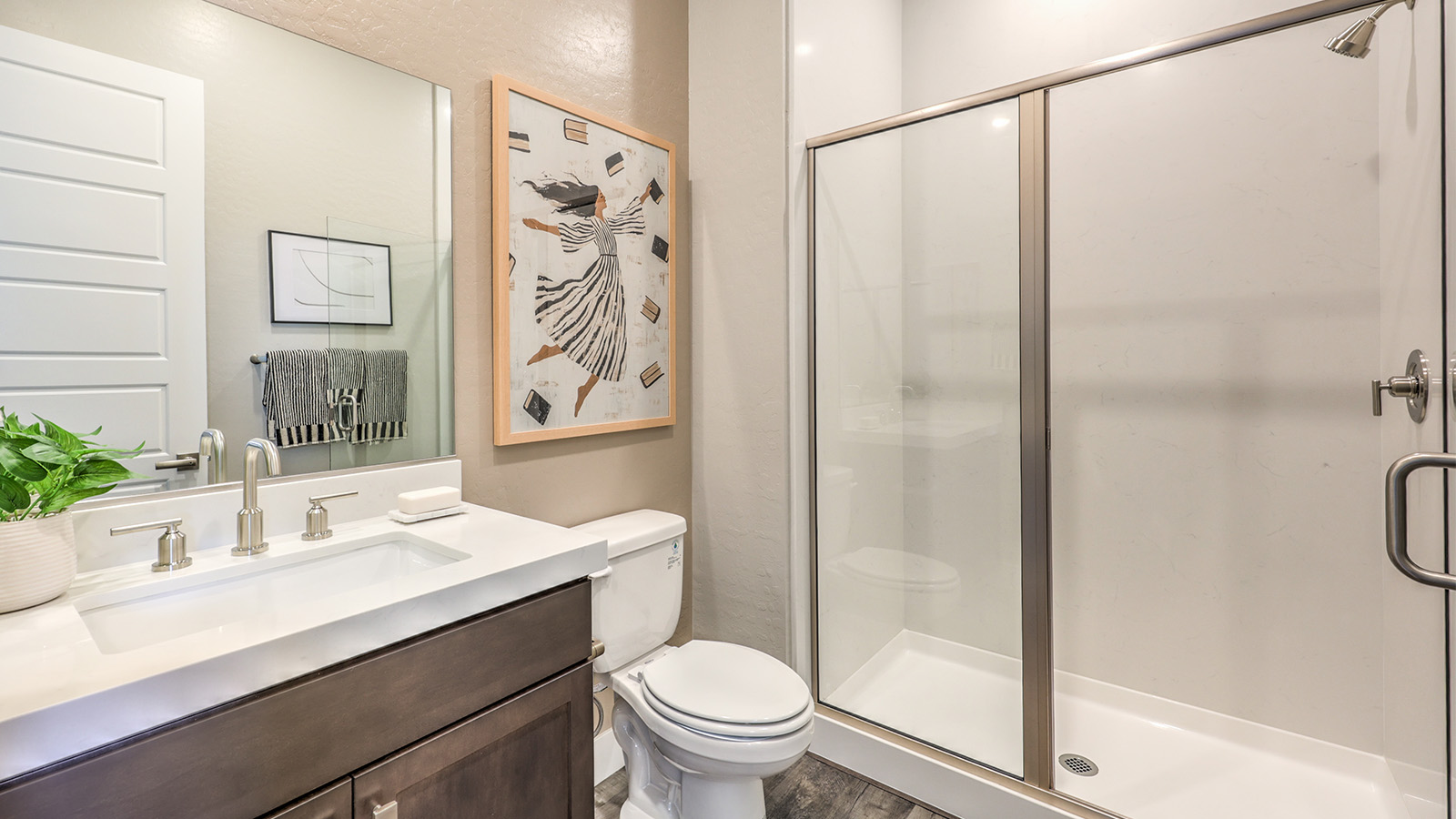 The second bathroom in our Heartland Manor 2538 Plan features luxury vinyl plank flooring, a vanity with quartz or granite countertops, and a combination shower and bathtub with a tiled surround. A large mirror enhances the space, while a high window allows natural light to brighten the room.