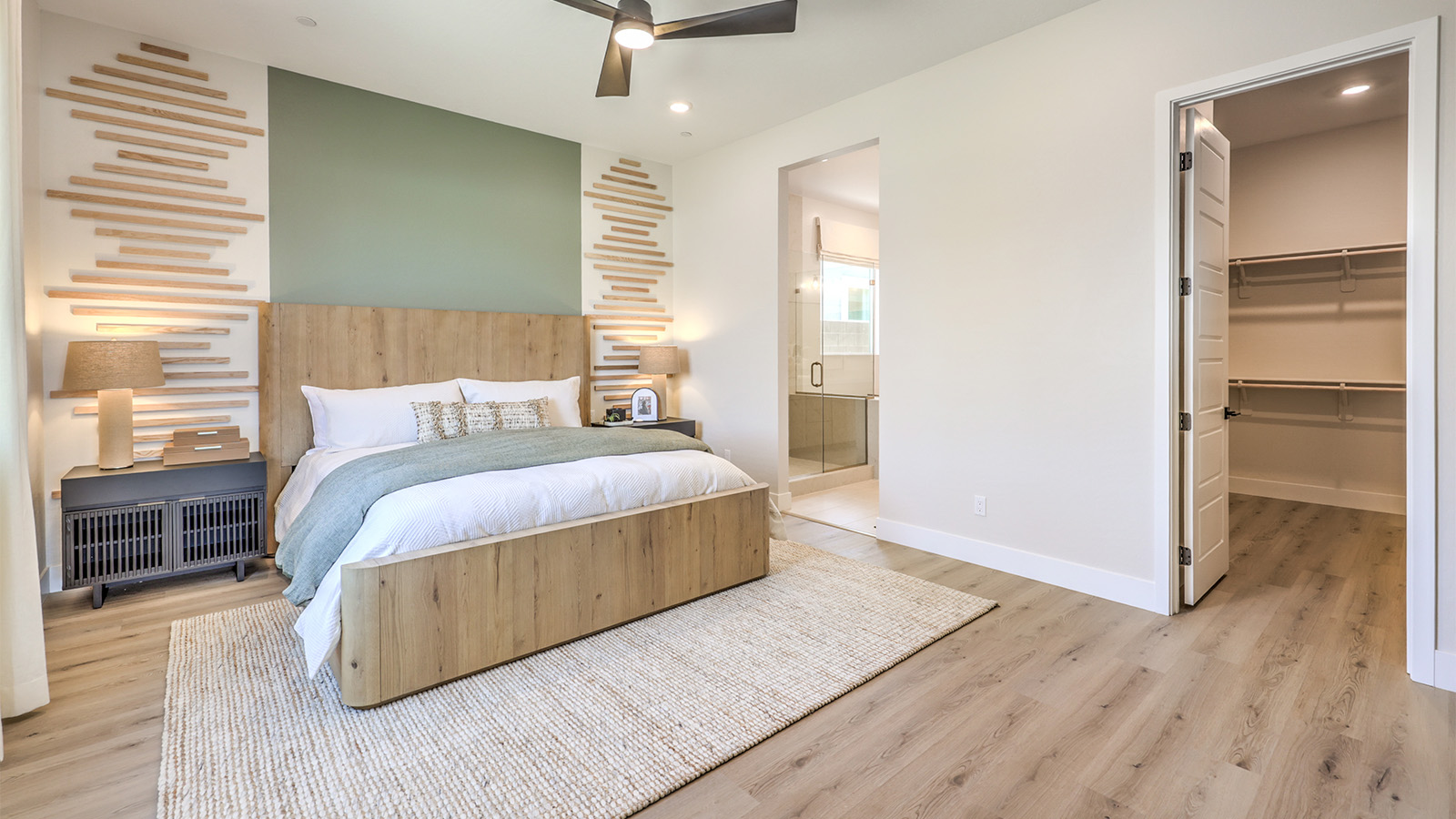 The main bedroom in our Heartland Manor 2754 Plan features plush carpet flooring, a spacious layout, and large windows that bring in natural light. A ceiling fan is centrally located for comfort, and an open doorway leads to the en-suite bathroom. The room also includes a walk-in closet, providing ample storage space.