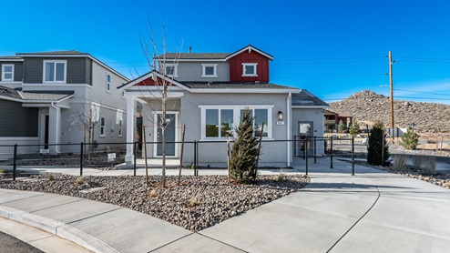 Exterior image of a model home in Reno's Phoenix community with gray stucco siding, red board-and-batten accents, and a covered front porch on a cul-de-sac.