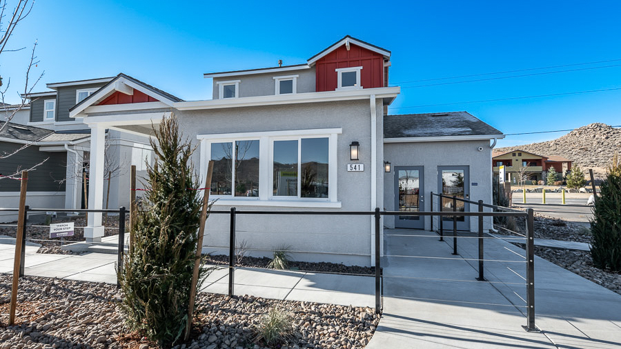 Exterior image of the Denali model home in Reno's Phoenix community with gray stucco siding, red board-and-batten accents, and a covered front porch on a cul-de-sac.