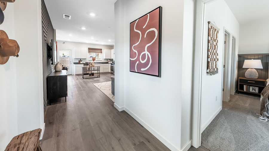 Front entryway of the Denali model home in Reno's Phoenix community with a long bench for seating and hats decorating the wall, with a peek through to the living room and kitchen and into the primary bedroom.