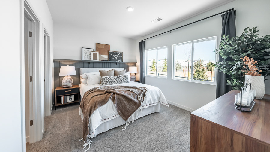 The primary bedroom in Phoenix's model home has two large windows allowing lots of natural light, a cozy bed flanked by lamp-topped nightstands, and a dresser.