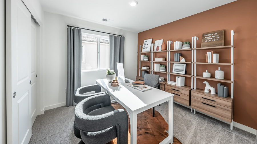 A secondary bedroom is set up as an office in Phoenix's model home with four bookshelves along the back wall and a sleek desk with a desk chair and two guest chairs.