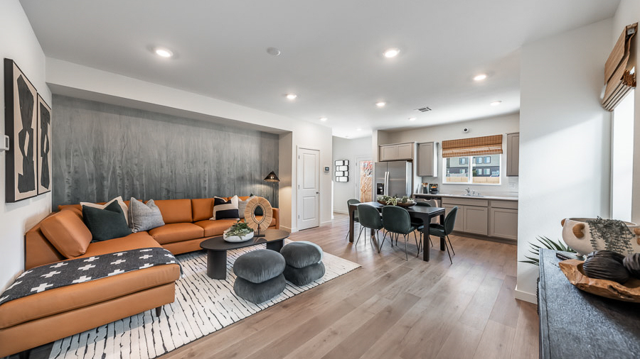 A living space in Phoenix's model home with a bold orange sectional sofa, coffee table, and two accent stools, a console table, and a view through to the kitchen and dining space.