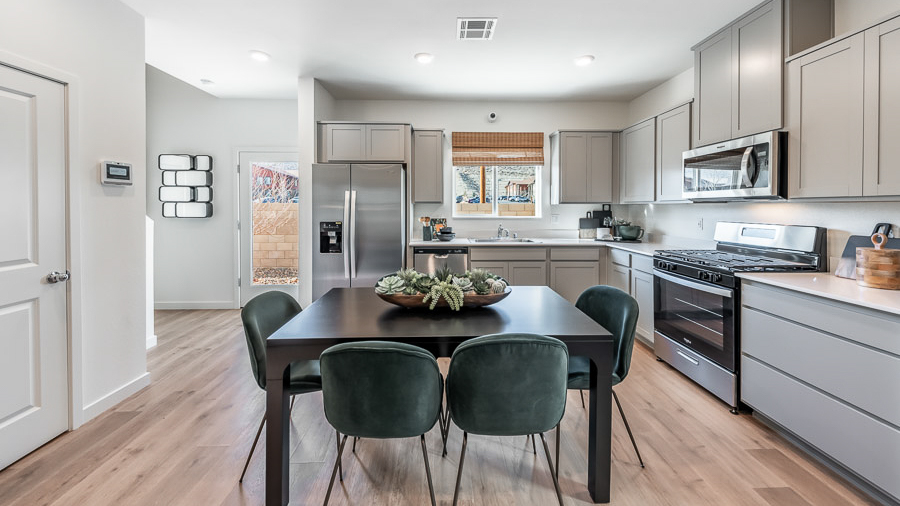 The kitchen in a model home in Phoenix with a dining table surrounded by 6 chairs in the center of the space and an L-shaped kitchen setup with gray, shaker-style cabinetry and stainless-steel appliances.