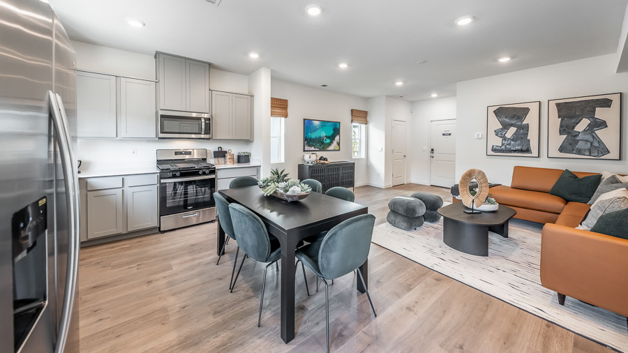 The kitchen in the Saguaro model home in Phoenix with a dining table surrounded by 6 chairs in the center of the space and an L-shaped kitchen setup with gray, shaker-style cabinetry and stainless-steel appliances.