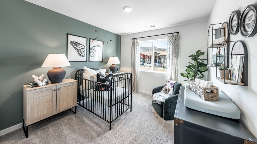 A secondary bedroom set up as a nursery with a crib, nightstands, a changing table, and a rocking chari in the corner, decorated with butterfly accents and artwork in a Phoenix model home.