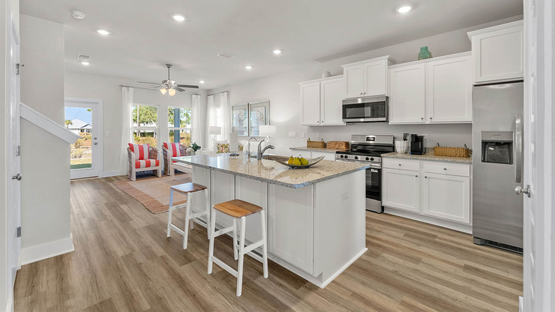 Kitchen with EVP flooring and granite countertops and white cabinets and island and stainless-steel appliances.