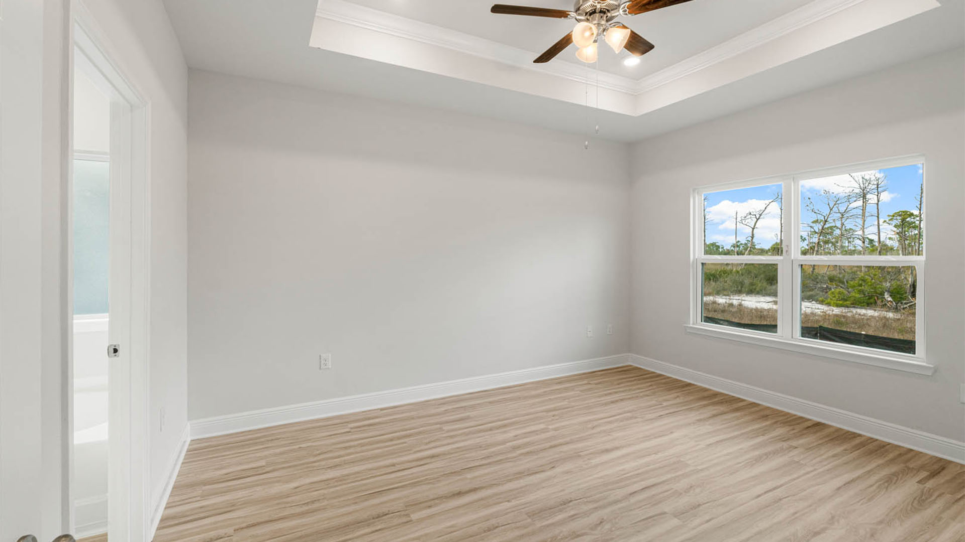 Primary bedroom with EVP flooring and tray ceilings and ceiling fan and two windows.