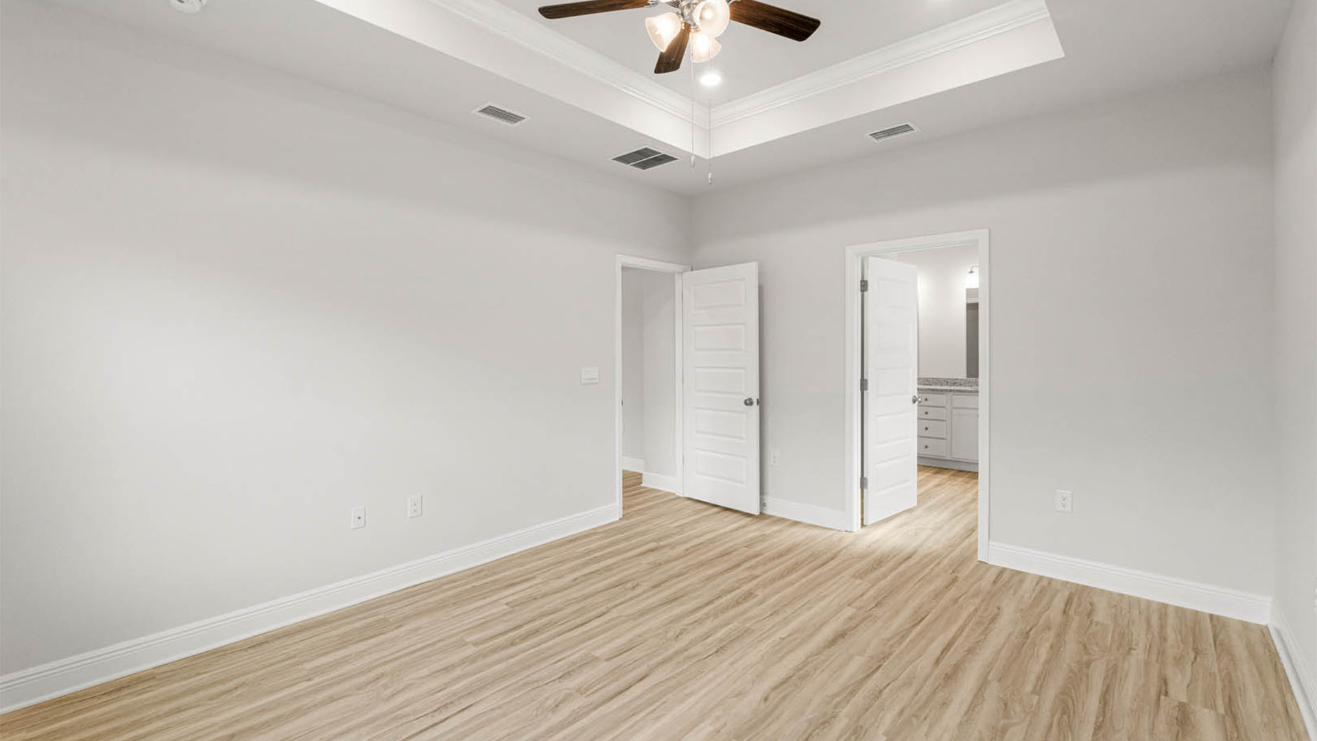 Primary bedroom with EVP flooring and tray ceilings and ceiling fan and bathroom entrance.