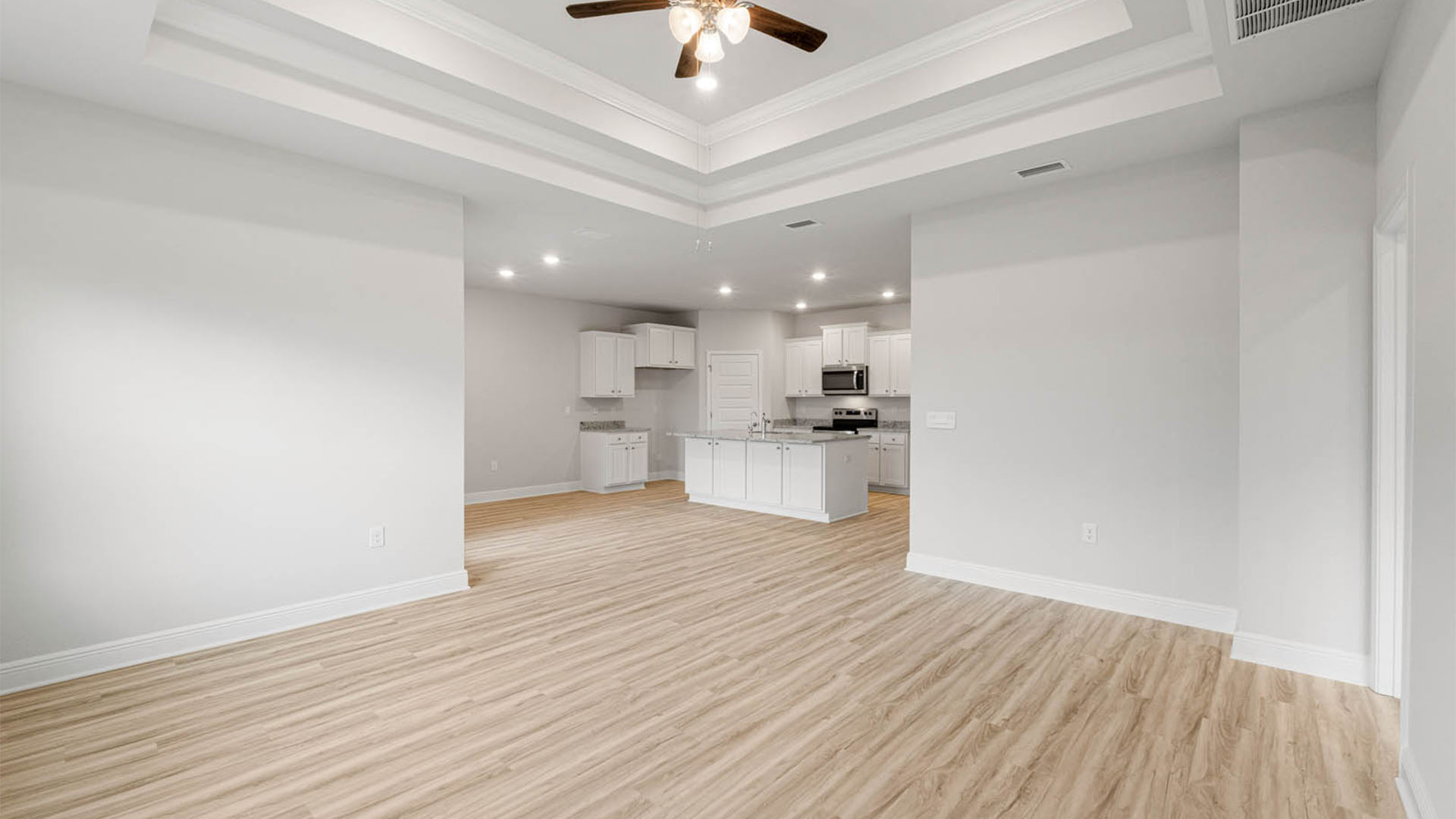 Open living room with tray ceilings and ceiling fan and EVP flooring and kitchen and dining area.