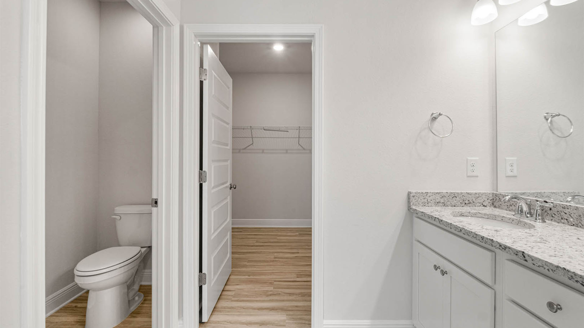Primary bathroom with double vanity granite countertops and toilet and walk-in closet with EVP flooring.