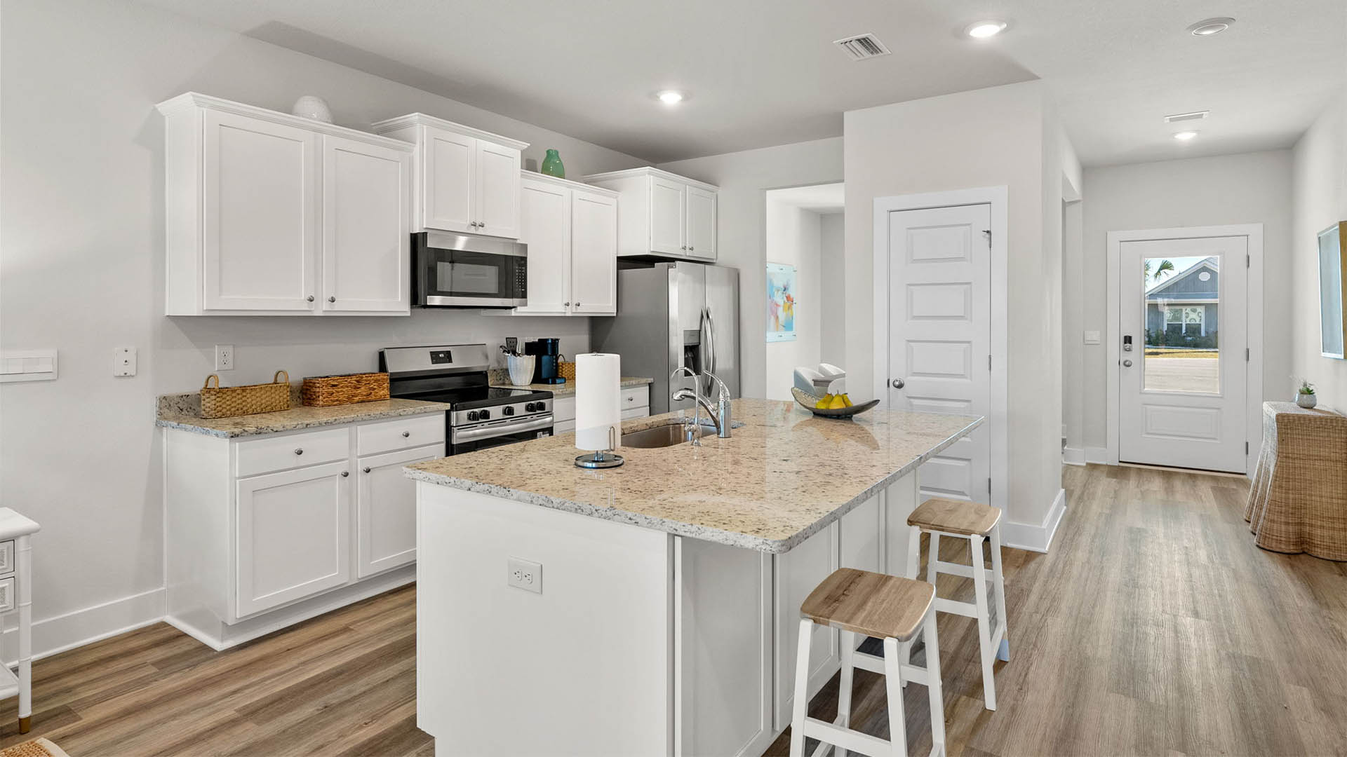Kitchen with EVP flooring and granite countertops and white cabinets and island and stainless-steel appliances.
