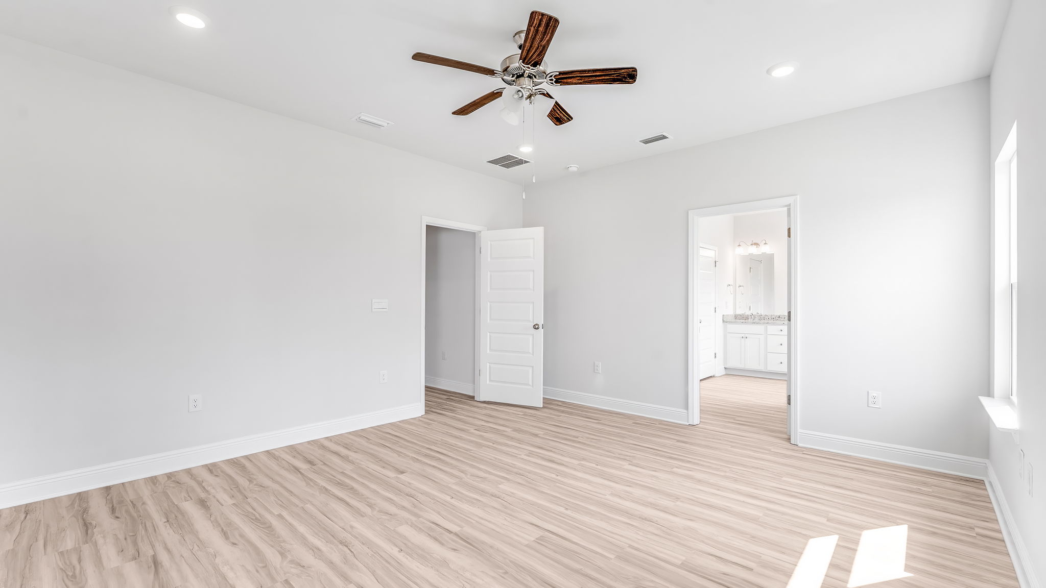 Primary bedroom with EVP flooring and ceiling fan and bathroom entrance.