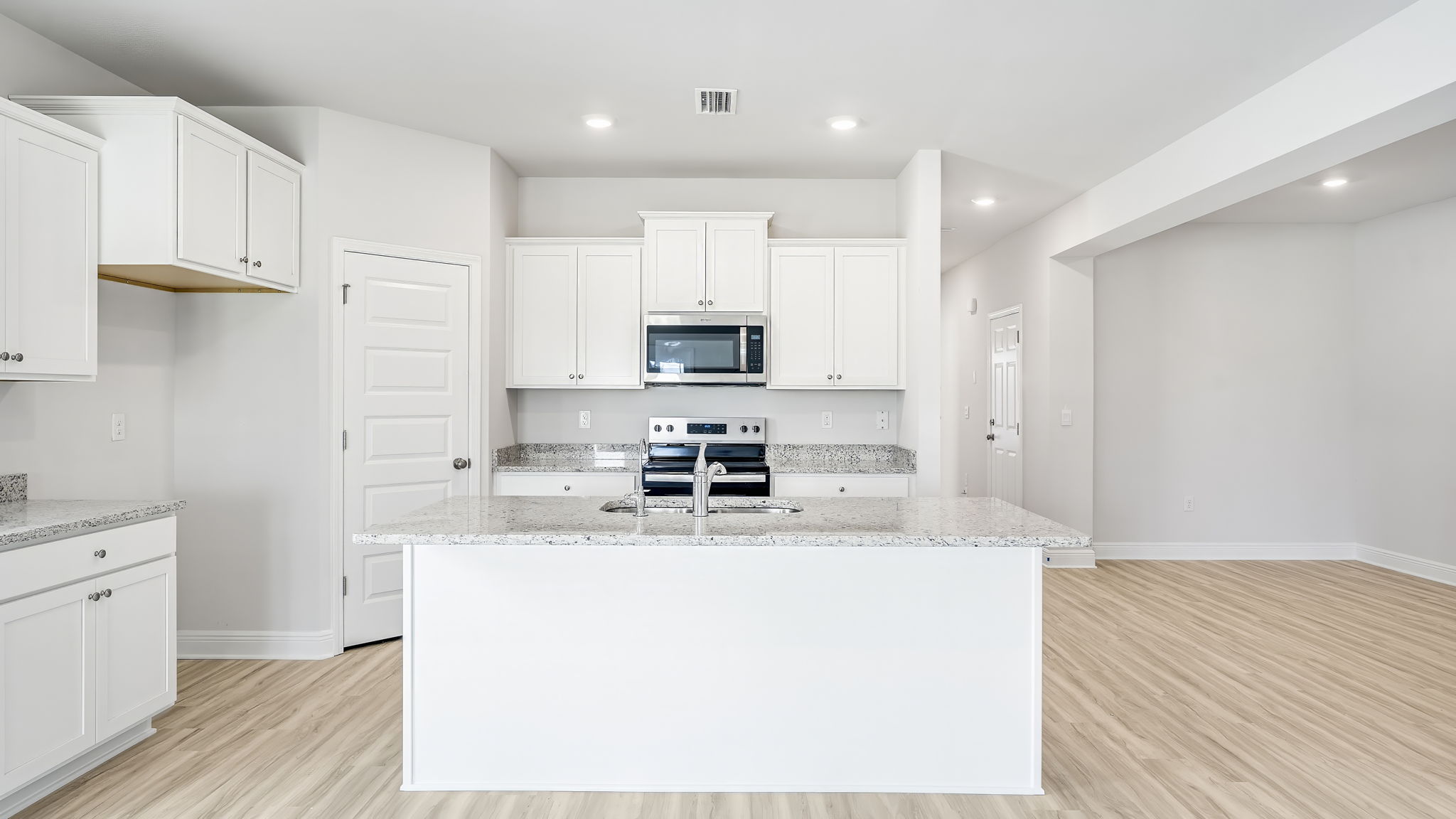 Open kitchen with EVP flooring and granite countertops and stainless-steel appliances and pantry.