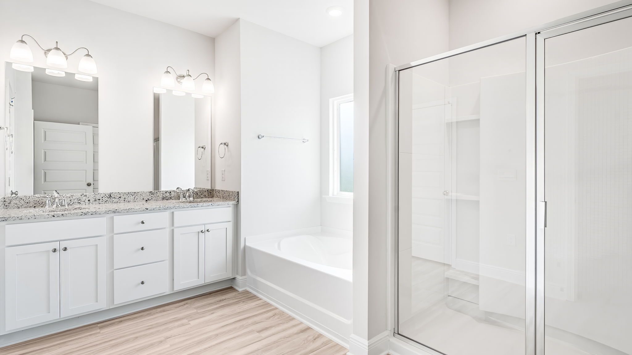Primary bathroom with double vanity granite countertops and separate tub and shower with glass door.