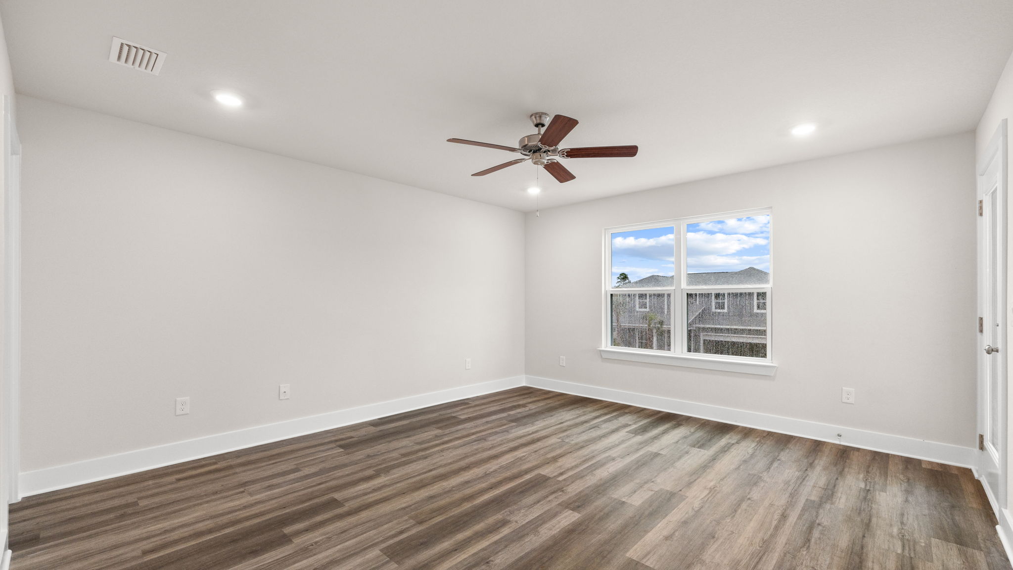 Primary bedroom with EVP flooring and balcony door and ceiling fan and windows.