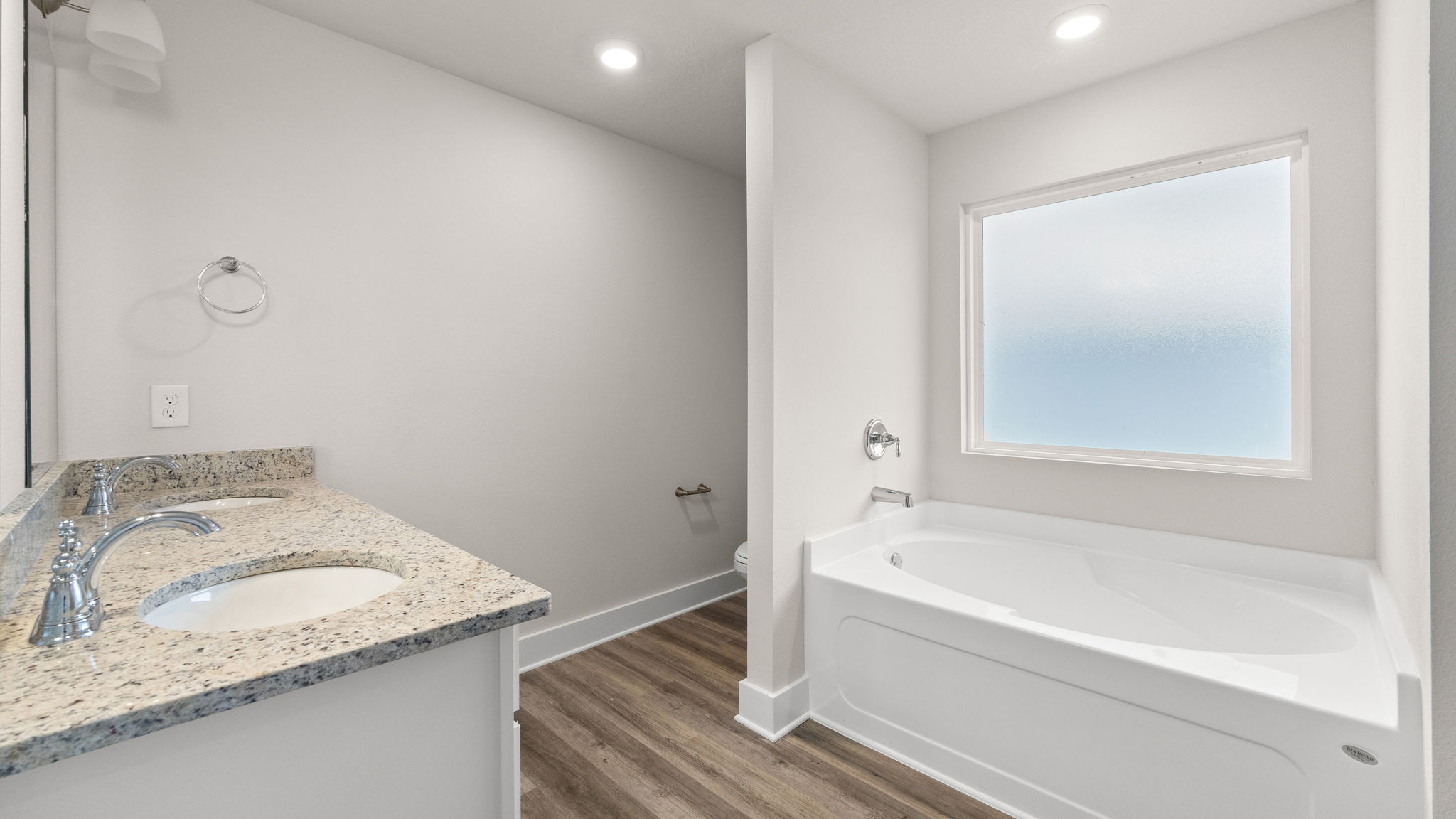 Primary bathroom with EVP flooring and double vanity granite countertops and white cabinets and tub and toilet.
