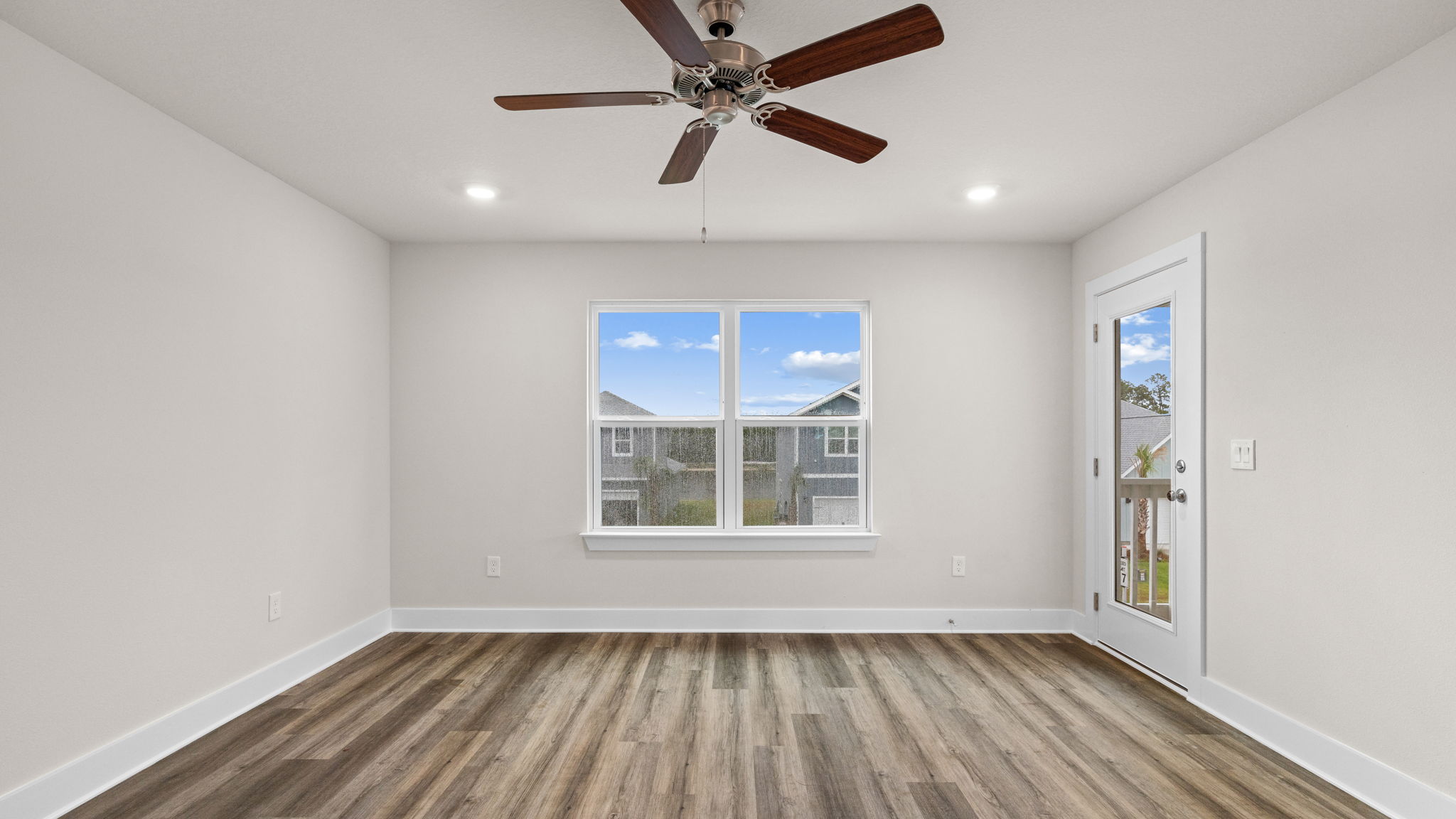 Primary bedroom with EVP flooring and balcony door and ceiling fan and windows.