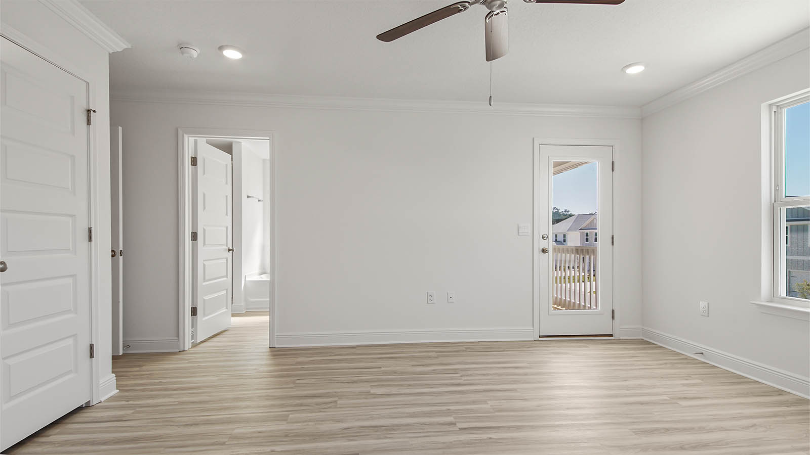 Primary bedroom with EVP flooring and balcony door and ceiling fan and bathroom entrance.