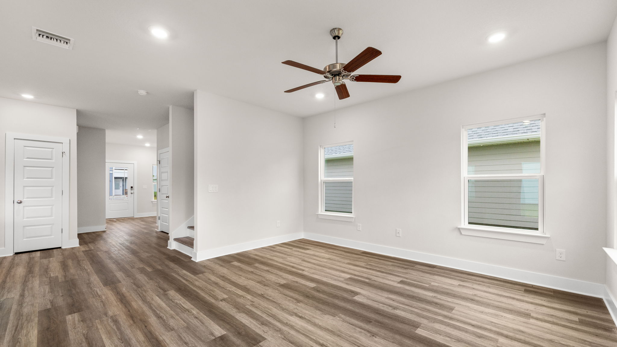 Living room with EVP flooring and ceiling fan and windows and stairs.
