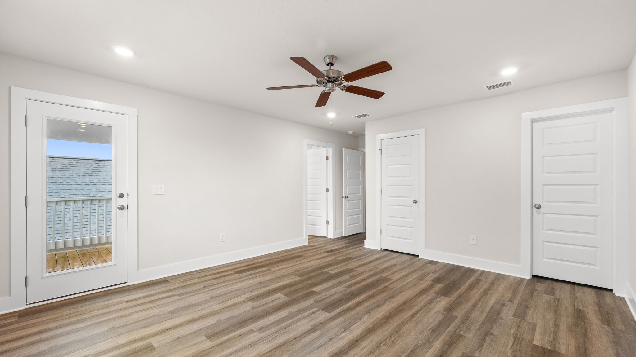 Primary bedroom with EVP flooring and balcony door and ceiling fan and closets.