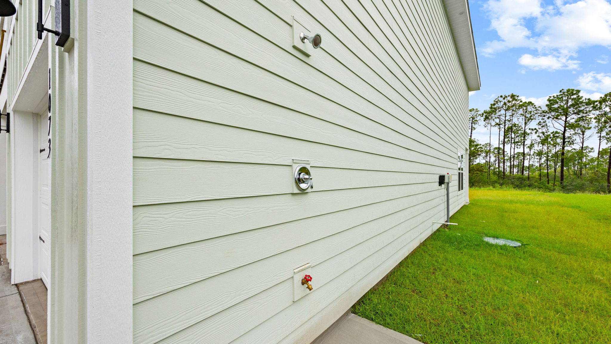 Outdoor shower on side of house next to garage.