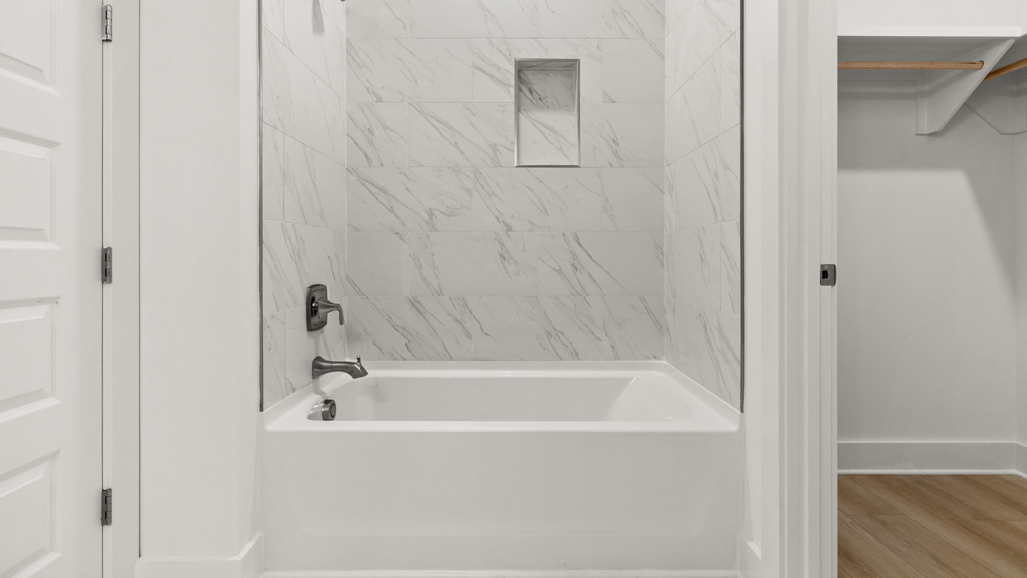 Bathtub with tile next to closet.