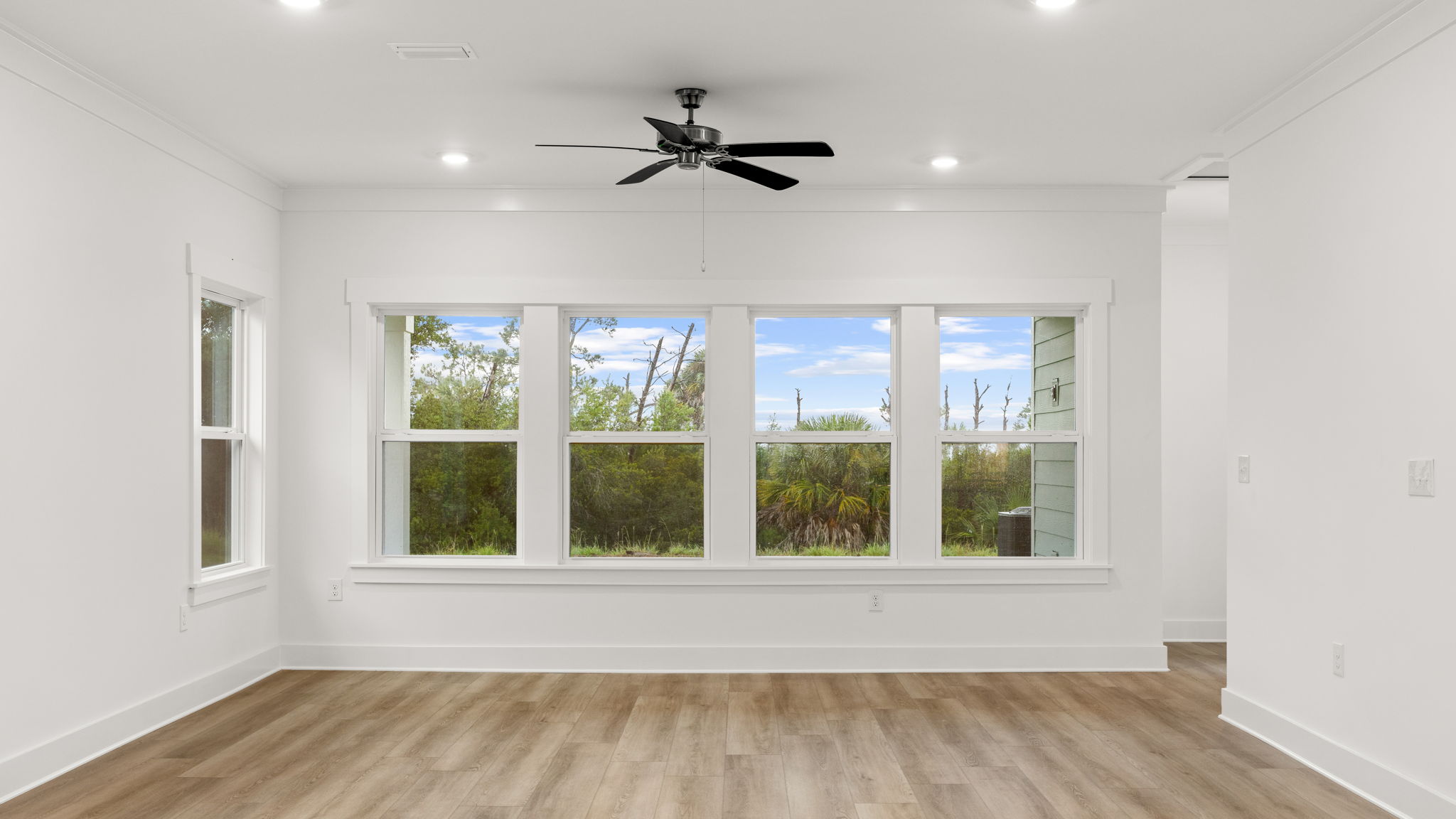Living room with ceiling fan and windows by primary bedroom.