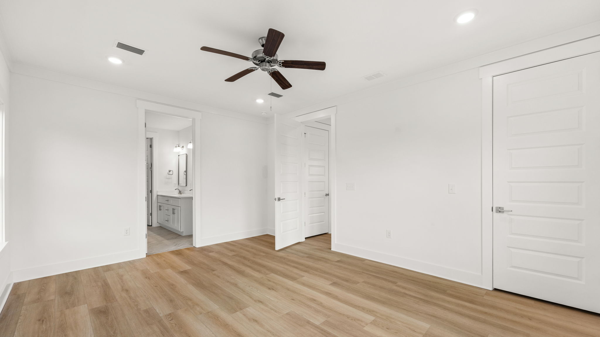Primary bedroom with ceiling fan and closet and bathroom entrance.