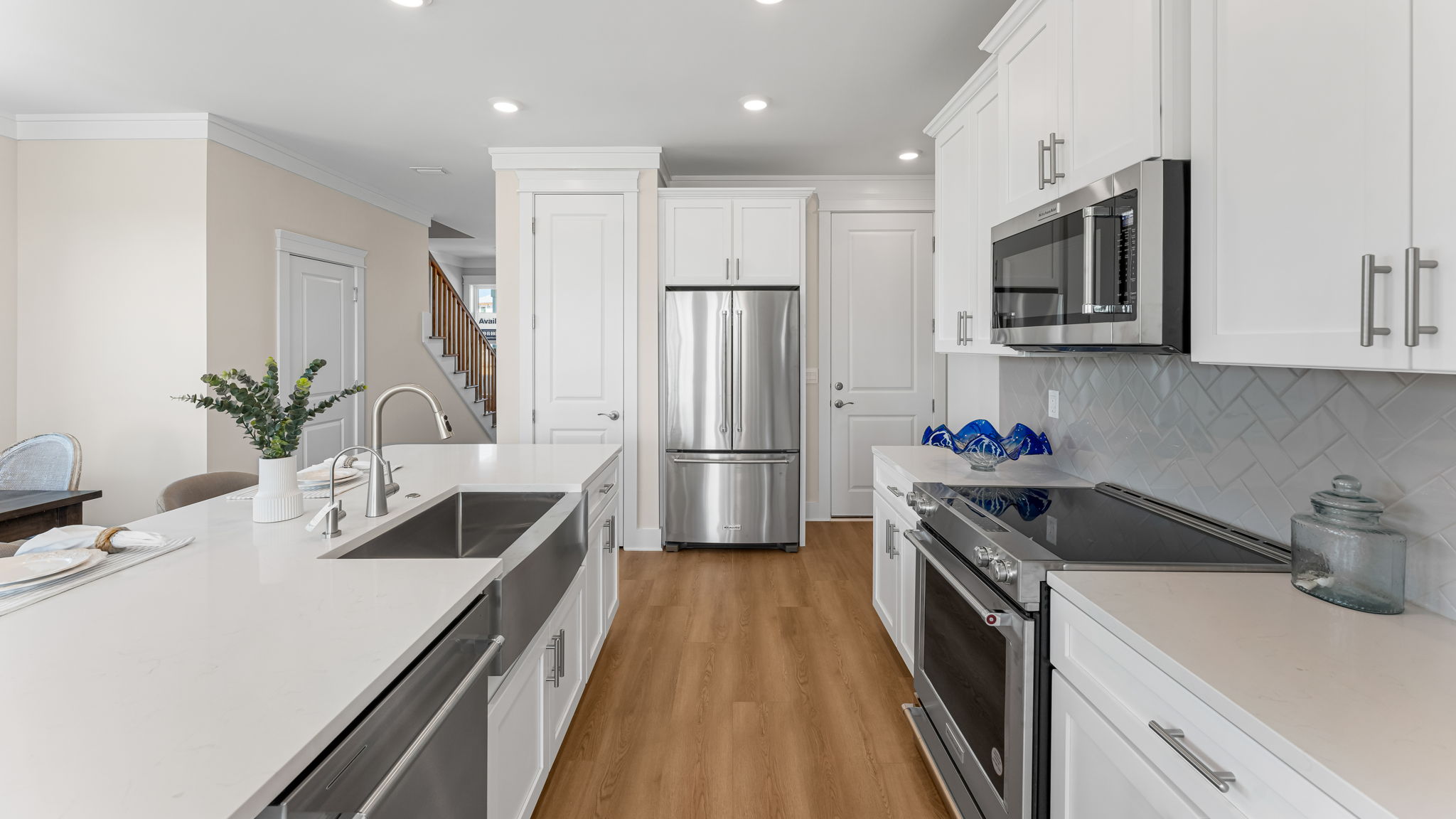 Open kitchen with island with quartz countertops and stainless-steel appliances and herringbone back splash and white cabinetry and pantry.
