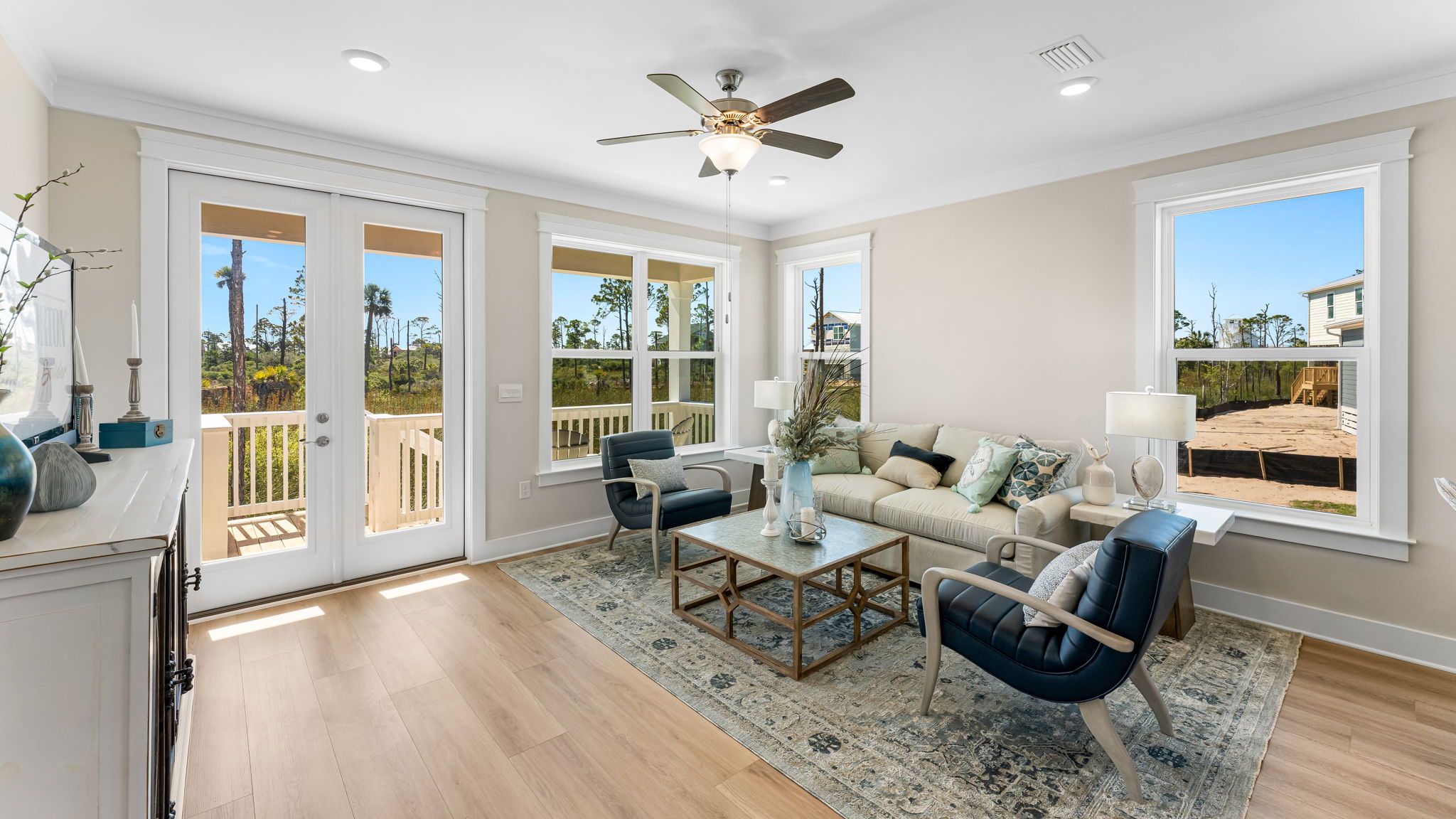 Open furnished living room with EVP flooring and ceiling fan and large windows and back door.