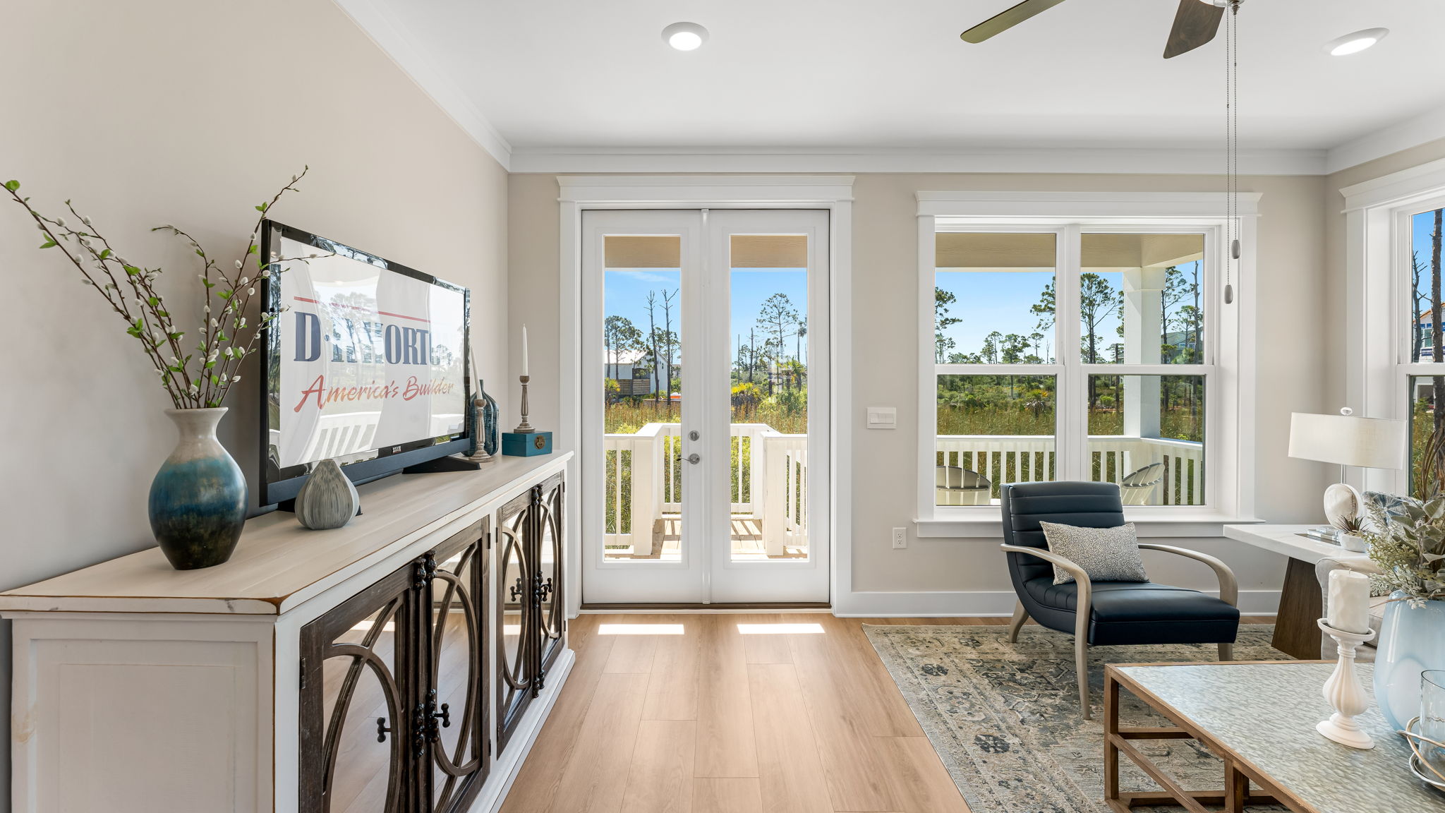 Open furnished living room with EVP flooring and ceiling fan and large windows and back door.